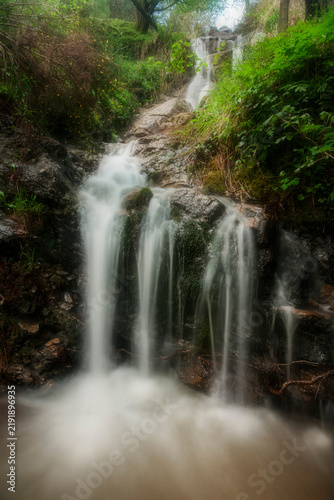 Small cascade in a forest stream surrounded by green mossy trees and nature in Montes de Triano mountain range, Bizkaia, Spain