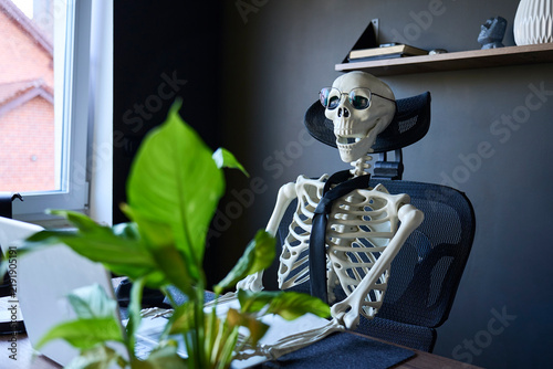 Foto Skeleton wearing glasses and tie sitting at computer desk in home office