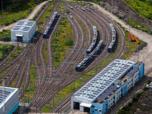 Aerial view of a train depot with multiple tracks and parked trains, featuring industrial buildings with solar panels on their roofs in Pune, Maharashtra, India.
