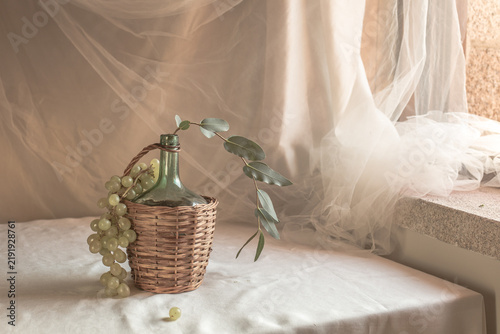 Cuadro en lienzo Elegant bright still life with a rustic wicker demijohn, fresh green grapes, and
