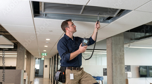 HVAC Technician Measuring Air Temperature at Office Vent
