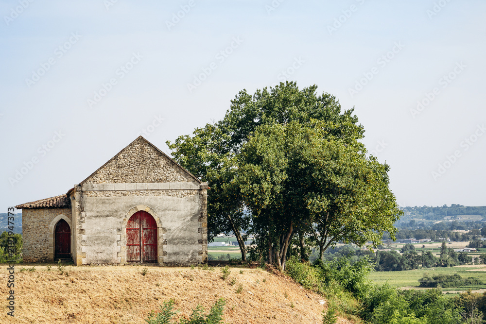 Fototapeta premium Rustic stone farm building with red wooden doors and trees in the vineyard countryside near Saint Emilion, Bordeaux wine region, France.