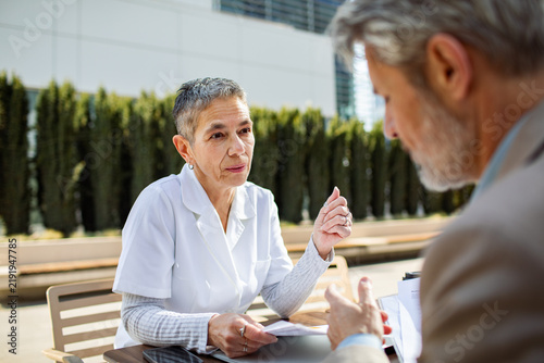 Senior nurse consulting with male patient outdoors at clinic