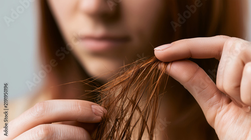 Woman examining dry, split and damaged hair ends with her fingers, close-up showing brittle strands and visible breakage near the tips, split ends, damaged hair, hair breakage, dry