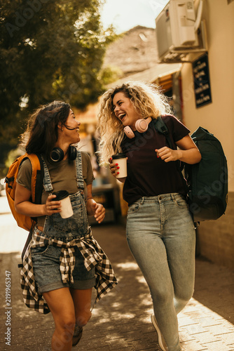 Two young female friends laughing walking on city street