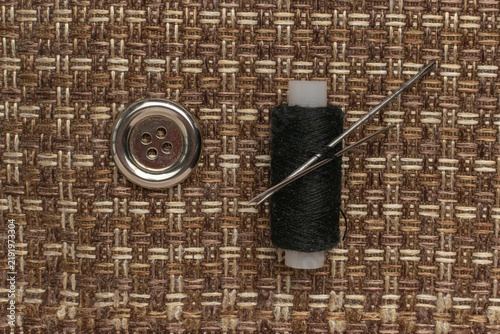 Foto Sewing Essentials: Button, Needle, and Thread on Rustic Woven Fabric