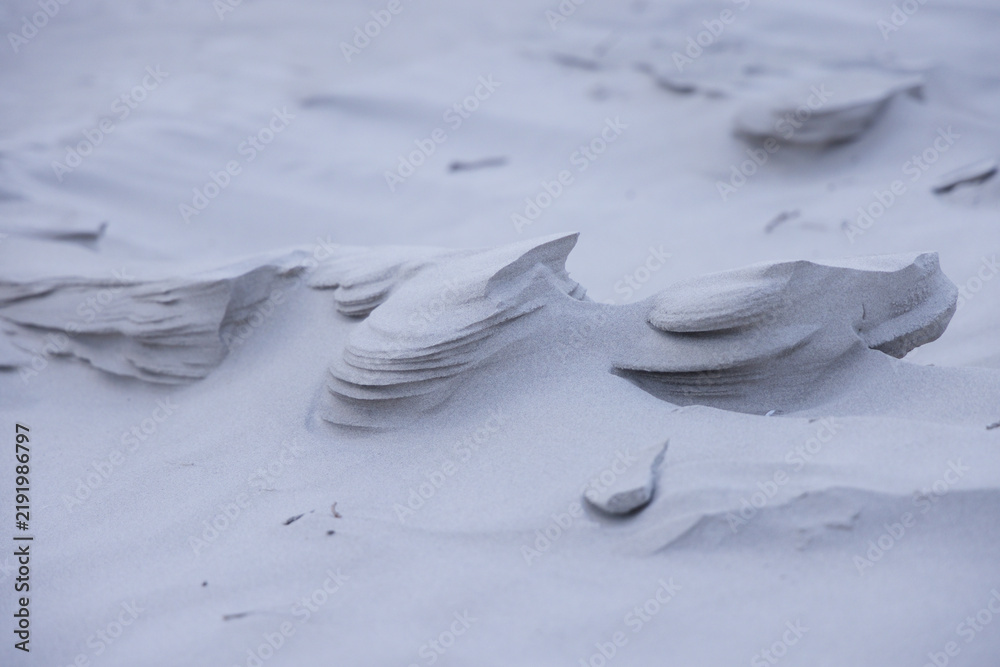 Obraz premium Wind-sculpted sand ridges are revealing layered overhangs on coastal dune, with scattered pebbles