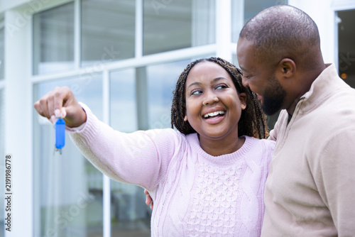 African American couple smiling, holding blue key fob and keys at modern home entrance