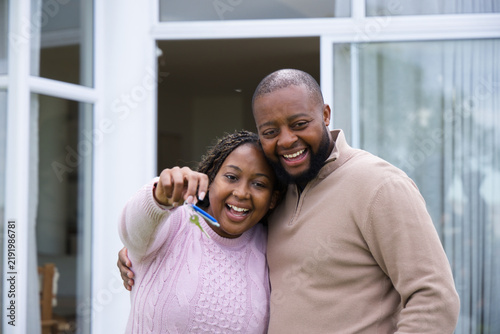 African American couple standing at home entrance, wearing sweaters, holding house keys and key fob