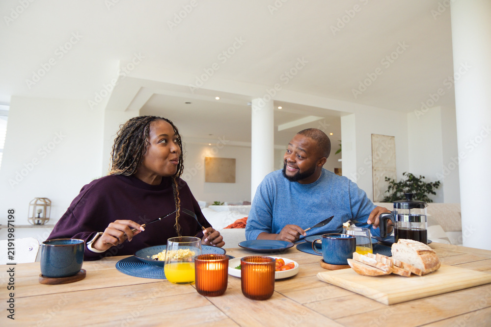 Obraz premium African American couple at home dining table in maroon blue sweaters sharing meal with French press