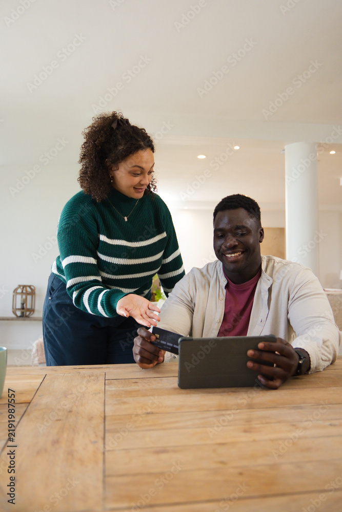 Obraz premium African American couple sitting at wooden table, man holding tablet with reader, woman handing card