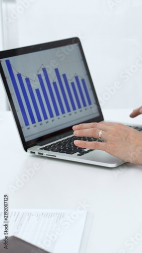 Businessperson analyzing financial charts on a laptop screen, typing on keyboard while reviewing data, working on reports for company growth, market strategy, and investment performance