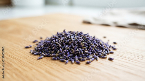 Fragrant dried lavender flower buds piled on a light wooden surface. Natural ingredient for herbal tea, aromatherapy, and relaxing crafts.