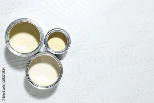 Quadro su tela Metal cans with paint in shades of beige on white wooden table, flat lay