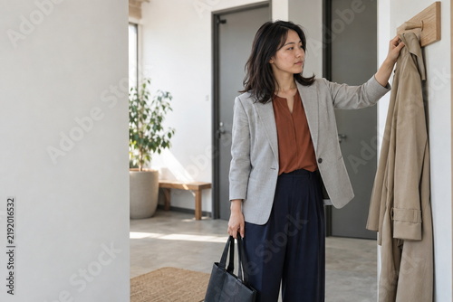 Plakat 仕事場の入口でコートを掛ける女性
