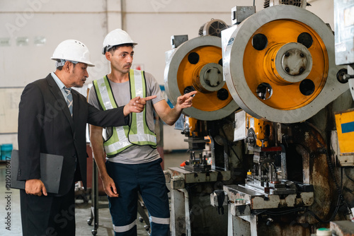 Industrial engineer and manager inspecting mechanical press inside manufacturing facility, discussing machinery operation, workplace safety, and production quality during collaboration