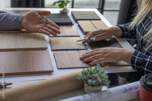Interior design teamwork cooperates on selecting variety of wood-textured samples for flooring or furniture materials.