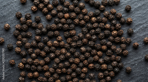 Принти на полотні Whole black peppercorns scattered on a dark textured slate surface