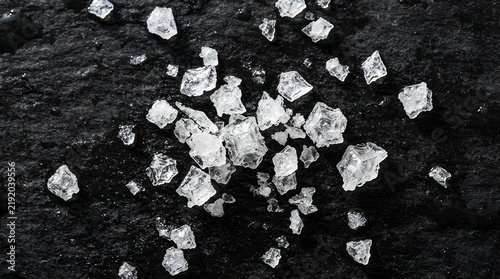 Coarse sea salt flakes scattered on a dark textured slate stone surface
