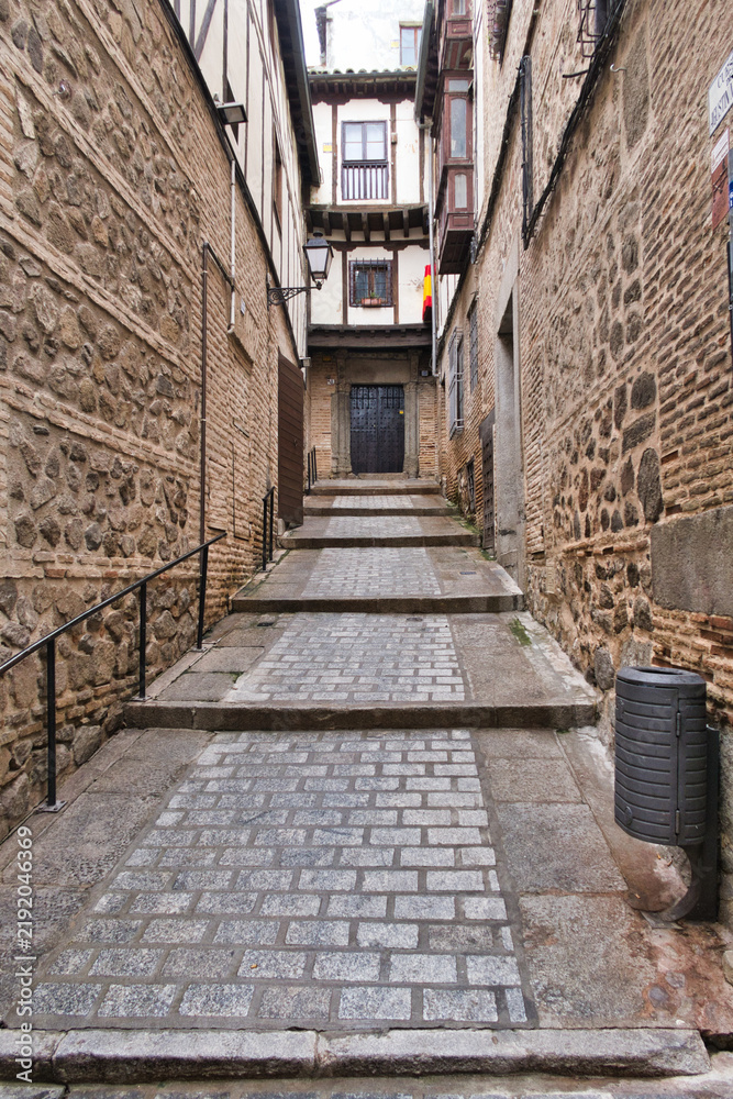 Fototapeta premium Historic Cobblestone Alleyway with Steps - A narrow, ancient alleyway with stone steps and traditional half-timbered buildings, leading to a dark wooden door in a European old town.