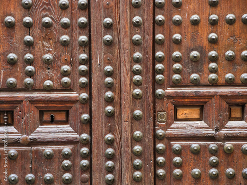 Ornate Old Wooden Door with Metal Studs - Close-up of a weathered, dark brown wooden door adorned with rows of decorative round metal studs and antique keyholes.