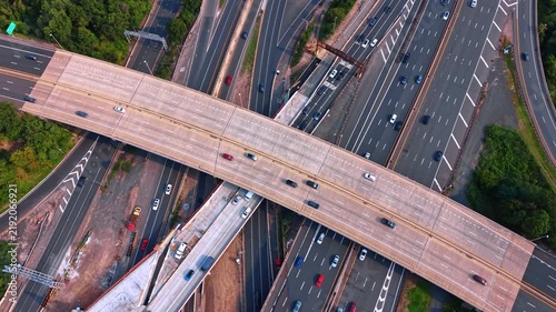 Footage over a massive multi-level highway interchange bustling with moderate vehicle traffic. A wide concrete overpass bridging over a dense network of multi-lane expressways running underneath.