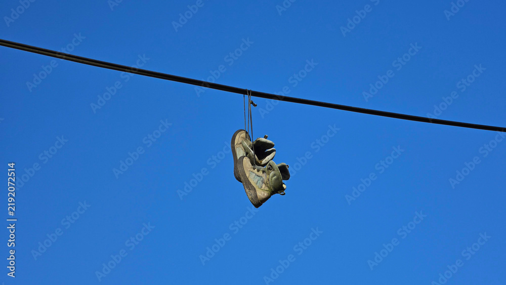 Obraz premium Pair of worn sneakers hanging by their laces over an overhead utility cable against a clear blue sky background