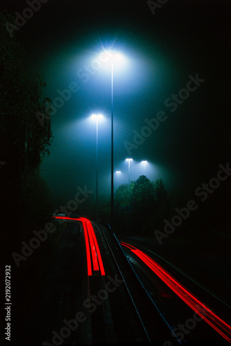 Foggy night, dark roadway with tail lights and high mast LED lighting with cold blue-white lighting in the mist