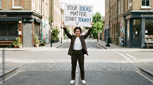 Person in a brown tailored suit holding a handmade motivational sign above their head on an empty street, white poster with casual hand lettering, bright daylight, centered full-body composition,