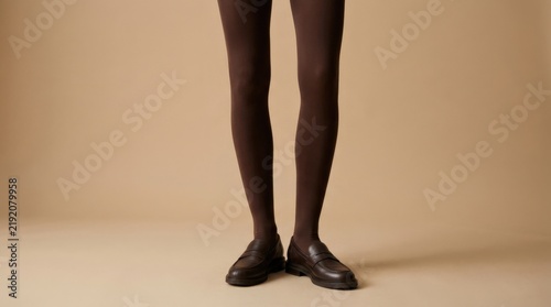 Cropped lower legs in deep brown tights against a warm beige studio background, minimalist fashion photography, strong vertical composition, soft even light, understated neutral palette, refined