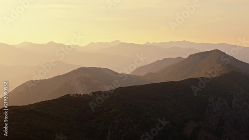 aerial drift above a forested mountain ridge at sunset with range after range of hills fading into golden haze, a calm moody b roll shot for titles and transitions, montenegro