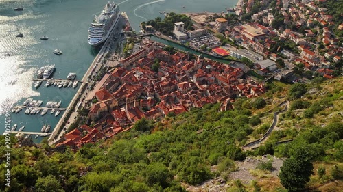 kotor, montenegro - aerial pull back over ruined fortress walls above kotor with the old town and marina below and bright sun glitter across the bay water