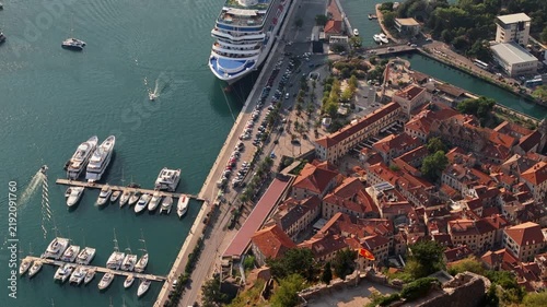 kotor, montenegro - aerial tracking view along the kotor waterfront promenade with parked cars, palm trees, yacht berths and a cruise ship at the quay in warm afternoon light