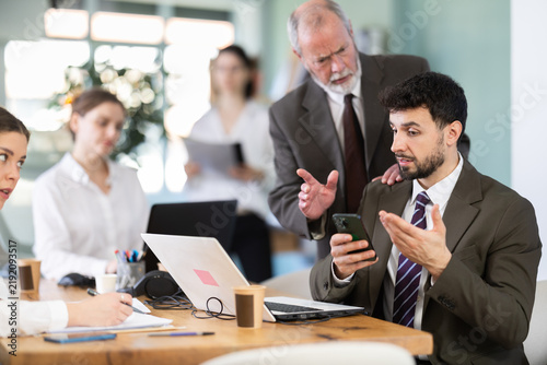 Quadro su tela Senior male boss chastises male subordinate for idleness and scrolling of phone, social networks and stealing personal and working time