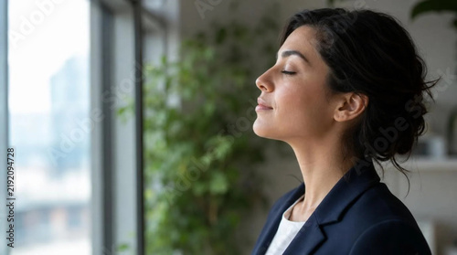 Side profile close-up of a calm young businesswoman by an open office window, eyes closed, taking a deep breath, meditation, mindfulness, wellness at workplace