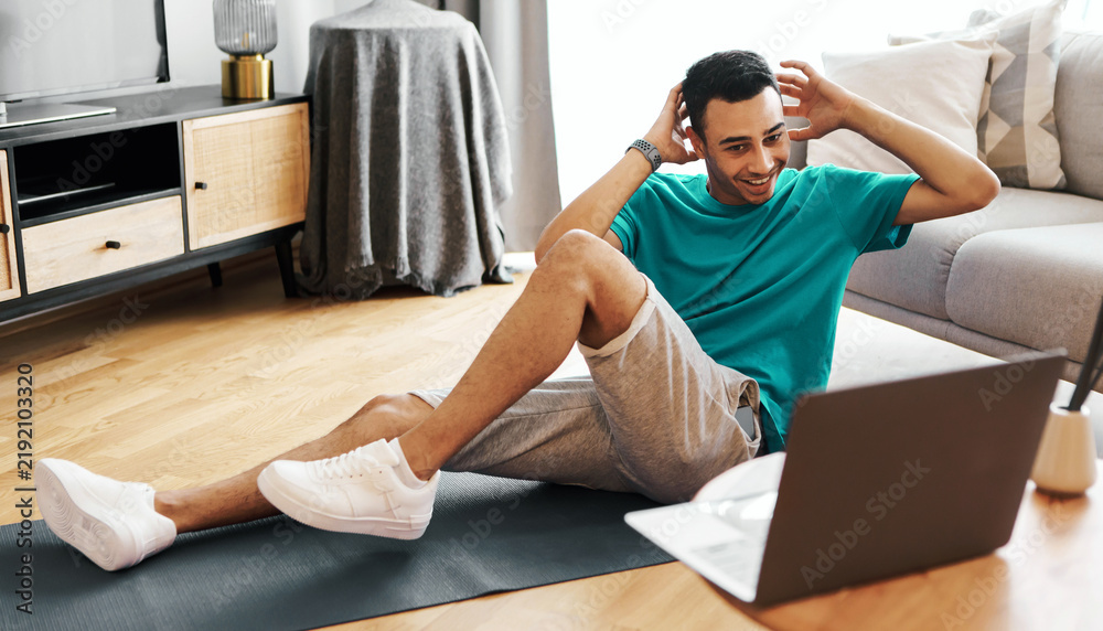 Fototapeta premium Happy Young Hispanic Male Doing Exercises While Working Out At Home On Mat, Focusing On His Fitness Routine In Modern Living Room, Engaged In Healthy Lifestyle.