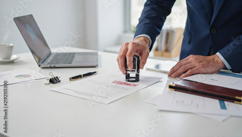 Fotografie Businessman stamping approved document with rubber stamp on desk with laptop and