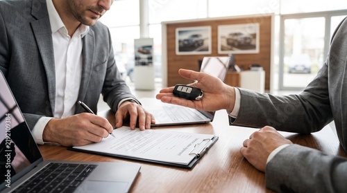 Professional client signing a significant business contract for a new vehicle purchase at a modern car dealership, finalizing the transaction and receiving the keys