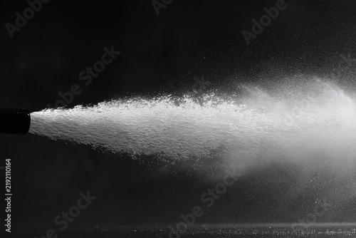 High-pressure water jet spraying outward from a dark nozzle against a dark background