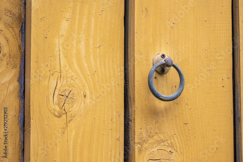 Obraz na płótnie A vintage round iron door knocker attaches to a weathered yellow wooden temple door with natural timber grain