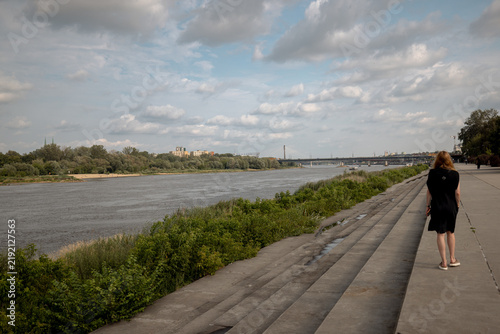 Canvastavla Warsaw, Poland - July 11, 2026: Pedestrian walks along the Vistula riverbank beside broad concrete steps and riverside vegetation in central Warsaw