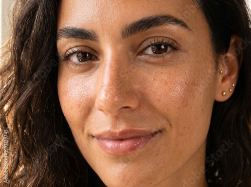 Close-up portrait of a young multi-ethnic woman with freckles and natural skin texture looking at the camera with a gentle smile