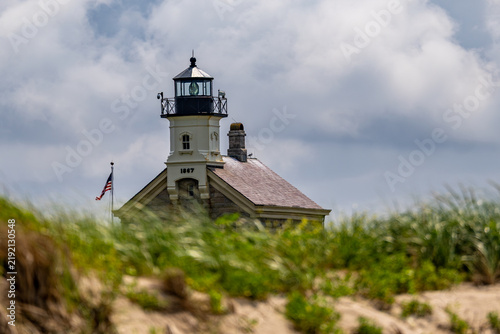Block Island North Lighthouse rising above the grassy headland, in the foreground under a cloudy sky.