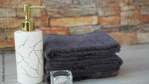 Foto Stacked dark gray towels and a liquid soap dispenser placed alongside a tealight candle, set against a blank background for text