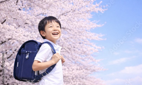 Plakat w ramie 満開の桜の下でランドセルを背負い笑顔で登校する日本人の小学生の男の子