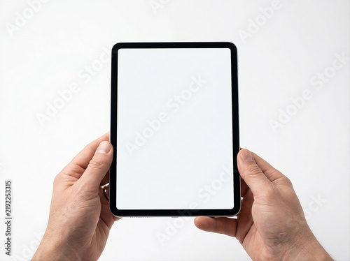Hands holding a digital tablet with blank screen mockup in portrait orientation against a neutral background