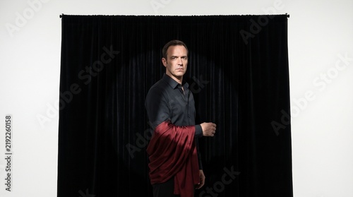 Man in dark shirt with red draped fabric posing against black curtain backdrop