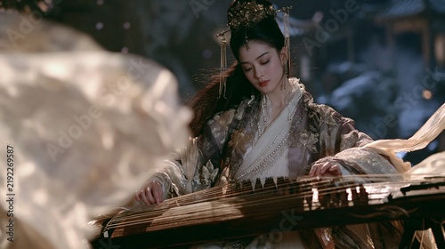 a woman in traditional Chinese attire, likely from a historical or cultural setting, plays a stringed instrument. She wears ornate headpieces with intricate designs and pearls, and her long.