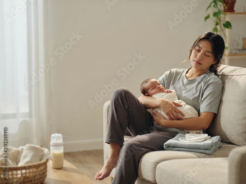 Exhausted Mother Sleeping While Holding Newborn Baby at Home