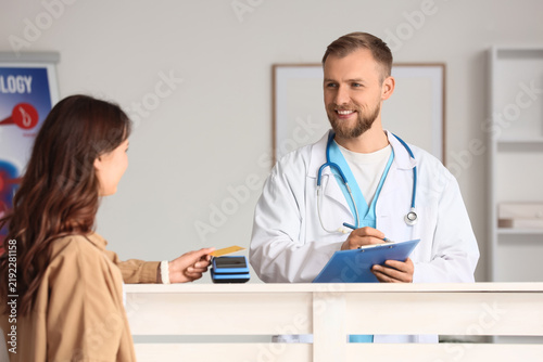 Young woman with credit card paying via terminal at reception in clinic